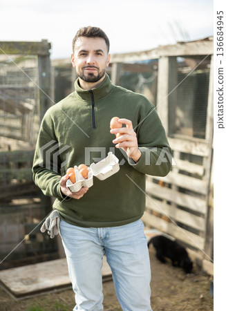 Positive man stands and holds in hands palms few fresh chicken eggs Positive man stands and holds in hands palms few fresh chicken eggs 136684945