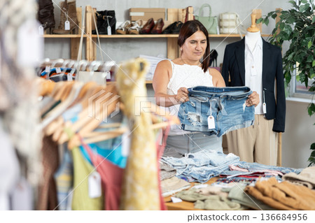 Latin woman customer turn over and choose denim shorts in store Latin woman customer turn over and choose denim shorts in store 136684956