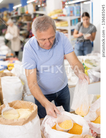 Old man purchaser buying crushed corn in big supermarket Old man purchaser buying crushed corn in big supermarket 136685045