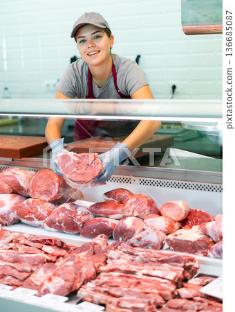 Young woman seller lays out beef in butcher shop 136685087