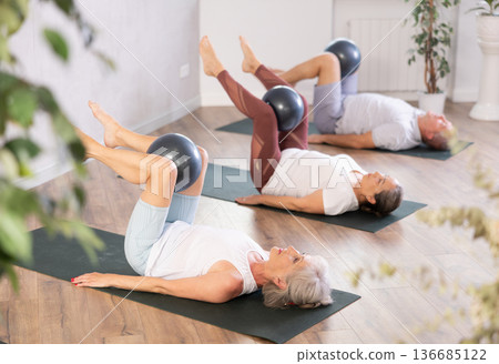 People lying on karemat, pulled bent legs to themselves and clamped soft-ball in knee People lying on karemat, pulled bent legs to themselves and clamped soft-ball in knee 136685122