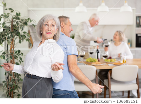 Senior man and woman doing couple dancing with their backs to each other during house party. Senior man and woman doing couple dancing with their backs to each other during house party. 136685151