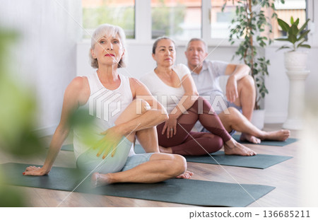 Women sitting on mats in pose Gomukhasana during yoga stretch joint workout in gym Women sitting on mats in pose Gomukhasana during yoga stretch joint workout in gym 136685211