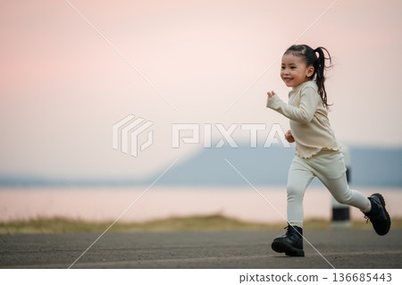 little child girl running happily on an open road by the water at sunset 136685443