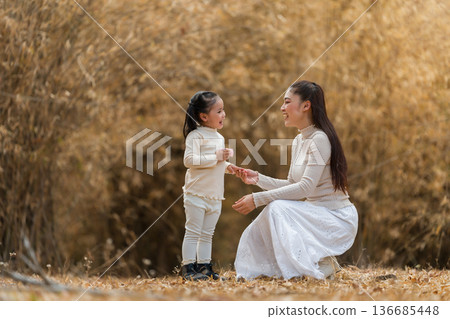 Mother teaching child girl how to use pink toy camera in the park or dry bamboo forest 136685448