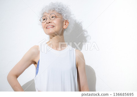 一位笑容可撻、頭髮花白的老婦人身穿夏季運動服或瑜珈服，抬頭望向前方。 136685695