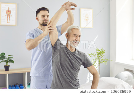A rehabilitation therapist helps an elderly man raise his arm, close-up A rehabilitation therapist helps an elderly man raise his arm, close-up 136686999