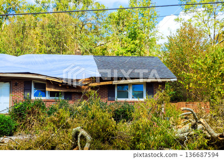 Storm damage shows fallen trees roof repairs on house in suburban area Storm damage shows fallen trees roof repairs on house in suburban area 136687594
