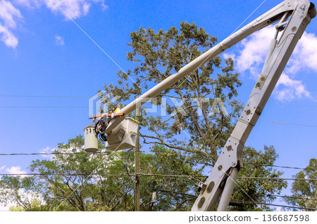 Worker performs maintenance on power lines using bucket truck in residential area 136687598
