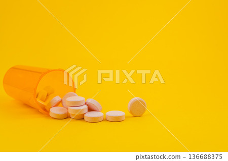 Pills spilled from a bottle on a yellow background 136688375
