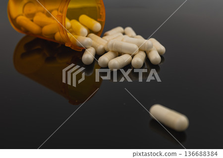 Capsules spill from an orange bottle on a shiny black surface 136688384