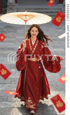 Young woman in red traditional dress holding umbrella with festive red envelopes flying around 136689342