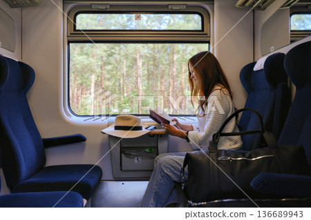 Woman reading book in train compartment with forest view 136689943