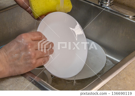 Washing Dishes With Sponge Under Tap 136690119