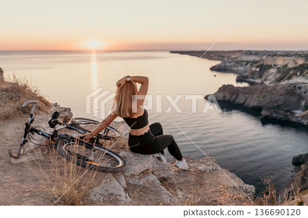 Woman bicycle sunset woman sitting on a cliff edge with a mountain bike overlooking a beautiful sea landscape during golden hour 136690120