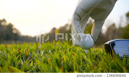 Golf ball on tee in a beautiful golf course with morning sunshine. Golf ball on tee in a beautiful golf course with morning sunshine. 136690640