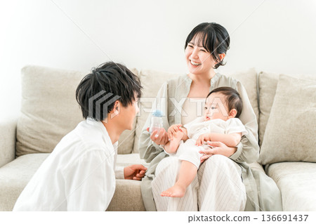 一位母親、一位媽媽和一家人坐在家裡的沙發上,用奶瓶餵寶寶。 一位母親、一位媽媽和一家人坐在家裡的沙發上,用奶瓶餵寶寶。 136691437