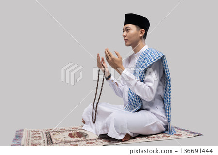 Man prays with beads raised. Man on prayer mat seeking spiritual illumination and peace 136691444