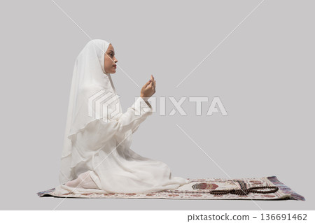 Serene woman kneeling with ritual. Woman in white headscarf performing silent ritual indoors Serene woman kneeling with ritual. Woman in white headscarf performing silent ritual indoors 136691462