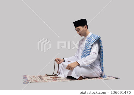 Person sitting with prayer beads. Man in meditation holding beads against simple background Person sitting with prayer beads. Man in meditation holding beads against simple background 136691470