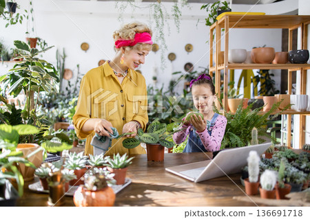 A mother and daughter enjoy tending to their plants together in a bright and airy greenhouse setting A mother and daughter enjoy tending to their plants together in a bright and airy greenhouse setting 136691718
