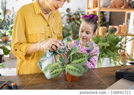 A woman and a young girl are shown caring for a potted houseplant, creating a heartwarming scene of nurturing and connection 136691721