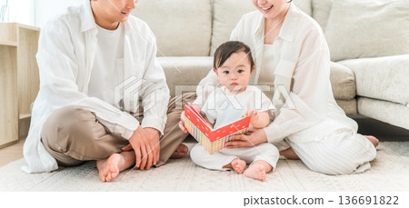 一對為人父母的夫婦在家裡的客廳裡唸圖畫書給孩子或嬰兒(育兒、親子互動、肌膚接觸) 一對為人父母的夫婦在家裡的客廳裡唸圖畫書給孩子或嬰兒(育兒、親子互動、肌膚接觸) 136691822