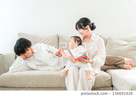 一對為人父母的夫婦在家裡的客廳裡唸圖畫書給孩子或嬰兒（育兒、親子互動、肌膚接觸） 136691826