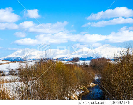A view of the Okigushi River and the Tokachi Mountain Range in Biei, Hokkaido, in winter under a clear blue sky A view of the Okigushi River and the Tokachi Mountain Range in Biei, Hokkaido, in winter under a clear blue sky 136692186