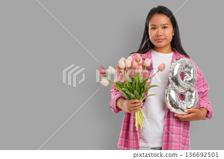 Young woman holds flowers and the number 8 for celebration Young woman holds flowers and the number 8 for celebration 136692501