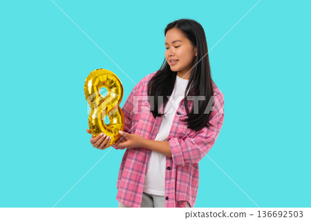 A young woman holds a gold number 8 while smiling A young woman holds a gold number 8 while smiling 136692503