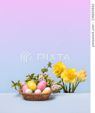 Multicolored Easter eggs in a basket with spring flowers: blooming spring cherry branches and yellow daffodils on gray table. Easter concept Multicolored Easter eggs in a basket with spring flowers: blooming spring cherry branches and yellow daffodils on gray table. Easter concept 136693682