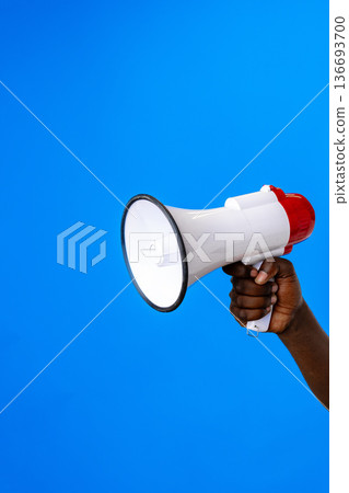 Loudspeaker held by hand against a bright blue background during a public speaking event Loudspeaker held by hand against a bright blue background during a public speaking event 136693700