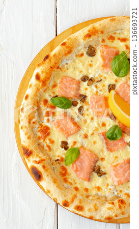 Fresh pizza with salmon, cheese, and basil on a wooden round board Fresh pizza with salmon, cheese, and basil on a wooden round board 136693721