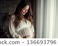 Beautiful pregnant woman touching her belly standing at home. 136693796