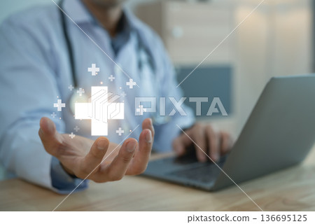 Doctor holding glowing medical cross icon over palm with laptop, Healthcare service and insurance concept 136695125