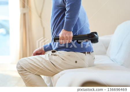 一位年長的亞洲男子正在用按摩槍按摩他的下背部 136696469