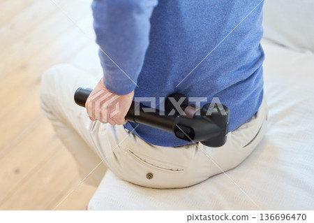 一位年長的亞洲男子正在用按摩槍按摩他的下背部 136696470