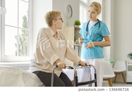 Senior patient using walker, nurse standing by to assist and help old woman Senior patient using walker, nurse standing by to assist and help old woman 136696726