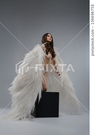 Ethereal woman with large white angel wings kneeling in an artistic studio portrait Ethereal woman with large white angel wings kneeling in an artistic studio portrait 136696758