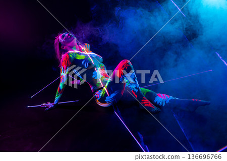 Sensual woman with fluorescent body paint posing in colorful smoke on dark background 136696766