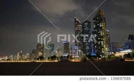 Nighttime city skyline with illuminated skyscrapers and clouds 136697086