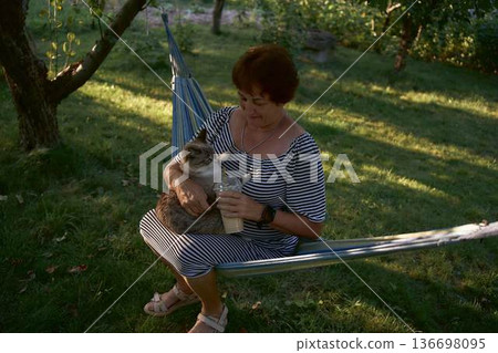 a senior woman relaxing in a hammock with thai blue tabby cat and bubble tea a senior woman relaxing in a hammock with thai blue tabby cat and bubble tea 136698095