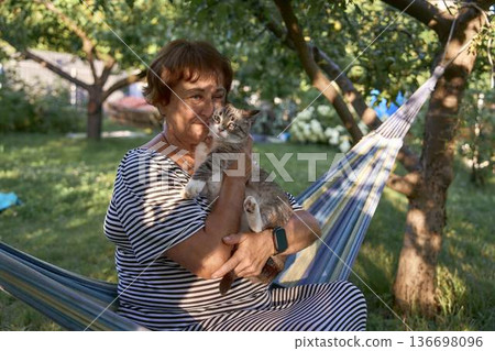 a senior woman relaxing in a hammock with thai blue tabby cat and bubble tea a senior woman relaxing in a hammock with thai blue tabby cat and bubble tea 136698096
