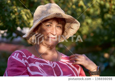 a senior woman in pink dress and straw hat enjoying golden hour sunset in the garden a senior woman in pink dress and straw hat enjoying golden hour sunset in the garden 136698098