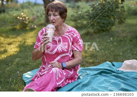 a senior woman relaxing on a picnic blanket with coffee in a summer garden a senior woman relaxing on a picnic blanket with coffee in a summer garden 136698103