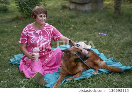 a Senior woman relaxing on a picnic blanket with german shepherd dog and coffee in a garden a Senior woman relaxing on a picnic blanket with german shepherd dog and coffee in a garden 136698113