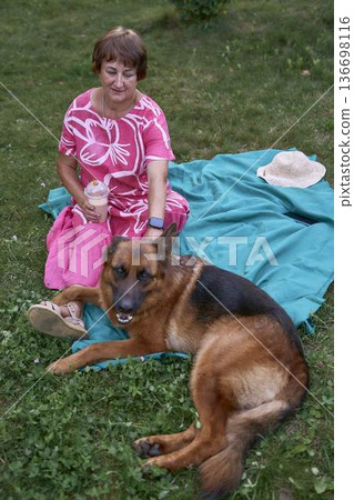 a Senior woman relaxing on a picnic blanket with german shepherd dog and coffee in a garden a Senior woman relaxing on a picnic blanket with german shepherd dog and coffee in a garden 136698116