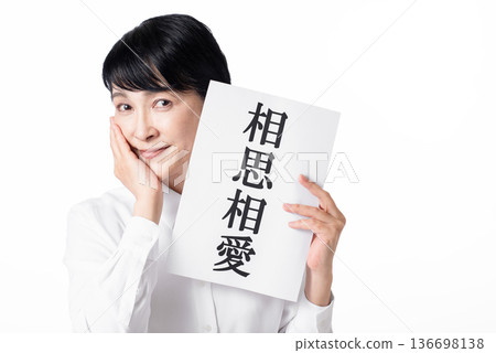 一位身穿白襯衫的老婦人,手裡拿著一張寫著「互相愛慕」的紙條,面帶微笑,一手撫摸著臉頰。 一位身穿白襯衫的老婦人,手裡拿著一張寫著「互相愛慕」的紙條,面帶微笑,一手撫摸著臉頰。 136698138