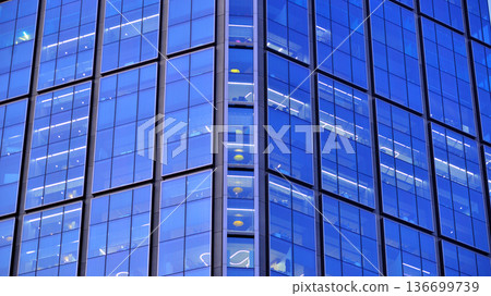 Big glowing windows in modern office building at night, in rows of windows light shines. Fragment of the glass facade of a modern corporate building at night. Modern glass office in city. Big glowing windows in modern office building at night, in rows of windows light shines. Fragment of the glass facade of a modern corporate building at night. Modern glass office in city. 136699739